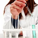 A woman wearing a lab coat using a dropper to drop liquids into a small beaker